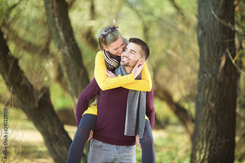 Young happy man carrying girlfriend on his back in park