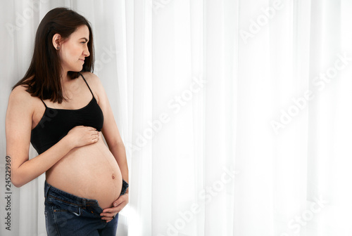 Young pregnant woman stands near the window at home Free Download Young pregnant woman stands near the window at home - GFXLoad