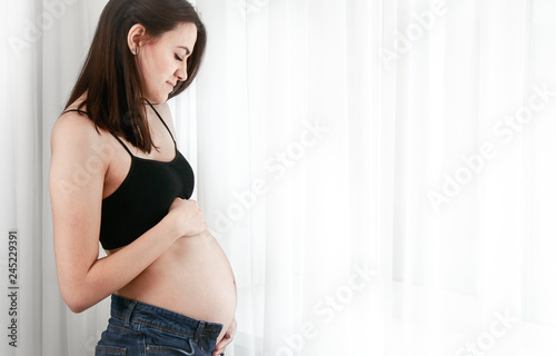 Young pregnant woman stands near the window at home Free Download Young pregnant woman stands near the window at home - GFXLoad