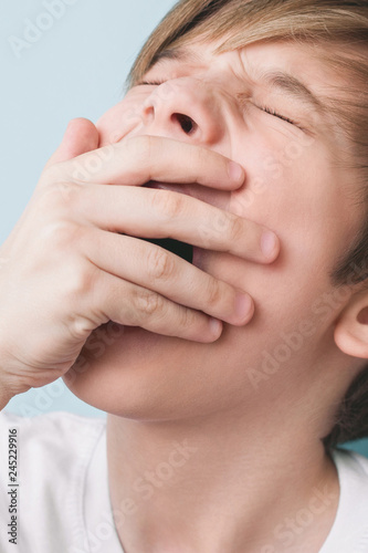 Boy yawns with his eyes closed, covering his mouth with his palm