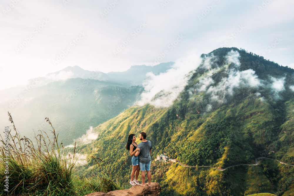 The couple greets the sunrise in the mountains. Boy and girl in the mountains. Man and woman hugging. The couple travels around Asia. Travel to Sri Lanka. Serpentine in the mountains. Honeymoon