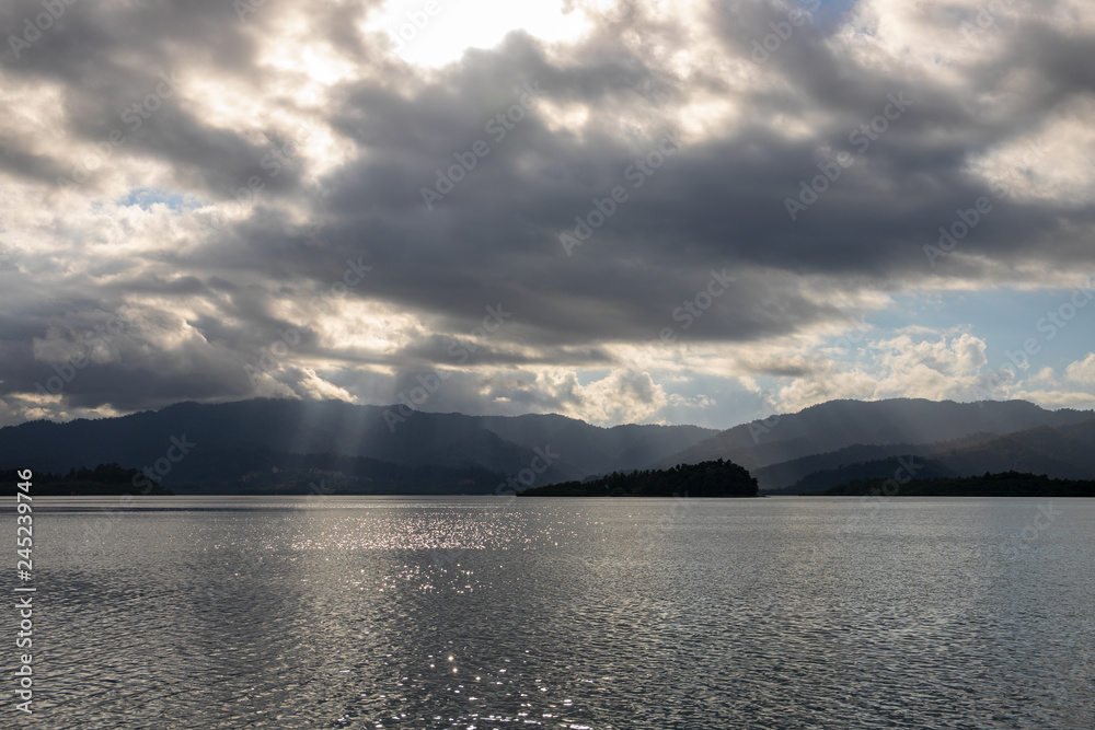 Cloudy sunset landscape with water and mountains. Distant islands in still sea. Sun beam on tropical island.