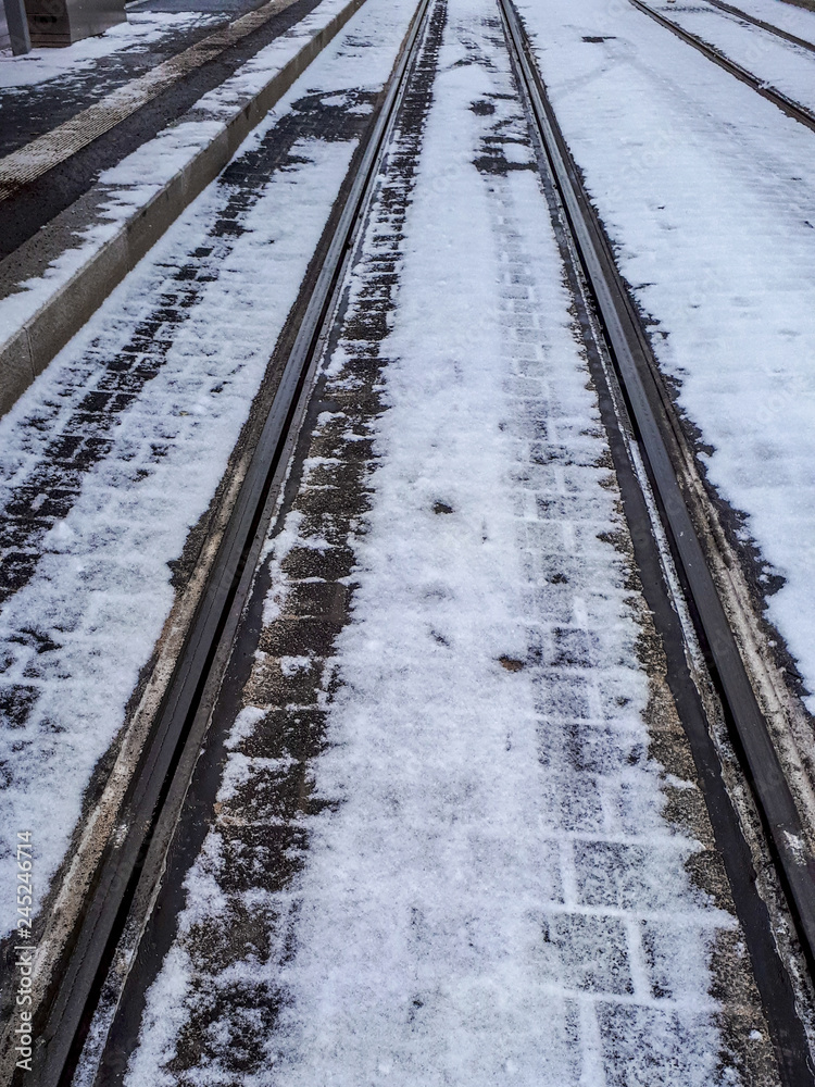 Fototapeta premium Pedestrian and railroad covered with snow in winter. Slippery cobble stones.