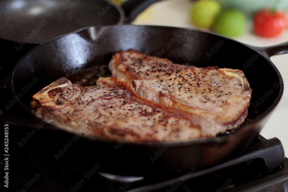 New York strip steaks frying in a cast iron pan on a natural gas stove top. New York strip steaks frying in a cast iron pan on a natural gas stove top.