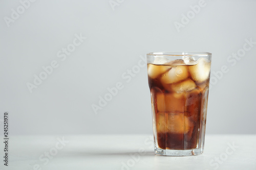 Glass of refreshing cola with ice cubes on table. Space for text