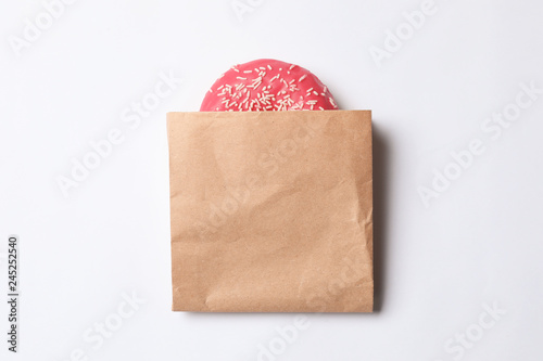 Paper bag with glazed doughnut on white background, top view. Space for design