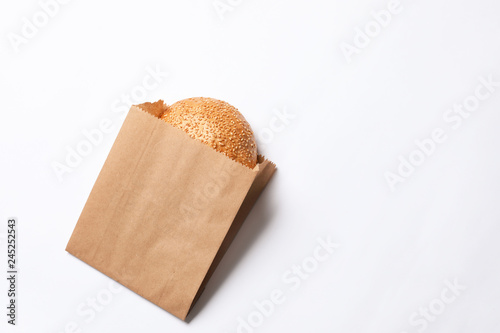 Paper bag with sesame bun on white background, top view. Space for text