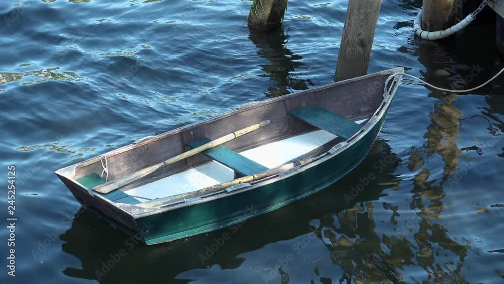 Old wooden row boat tied up to an old wooden dock in a scenic and peaceful harbor in New England