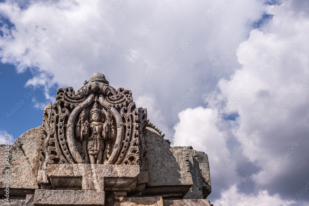 Belavadi, Karnataka, India - November 2, 2013: Veera Narayana Temple. Vishnu statue on the front top of One of the three Vimana Towers against heavy cloudscape in blue sky. 