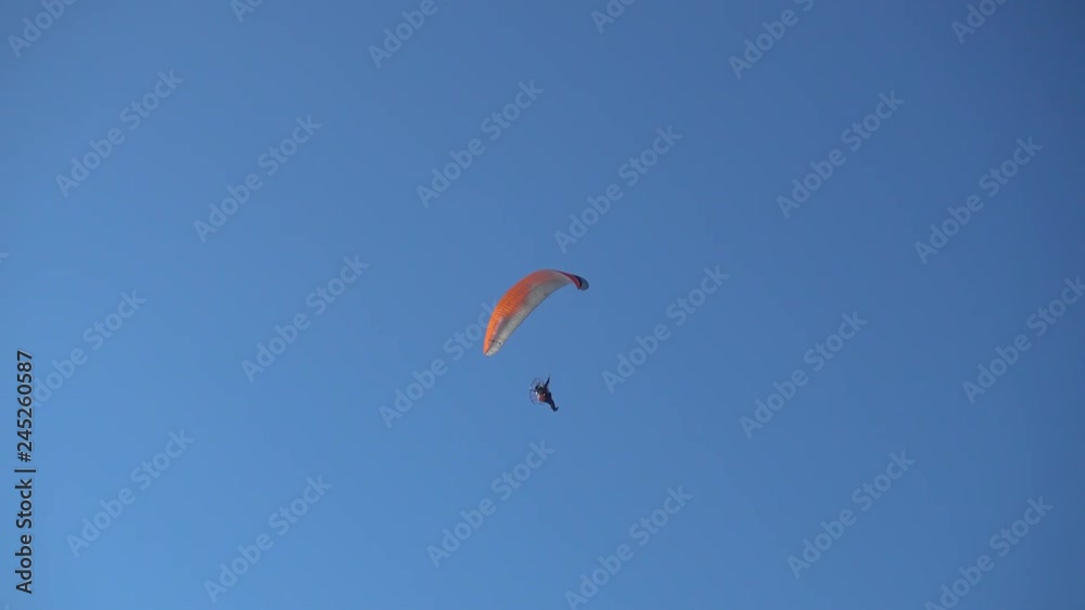 A motor paraglider, flies in the blue sky of a clear, sunny day passing in front of the sun. A motor paraglider, flies in the blue sky of a clear, sunny day passing in front of the sun.