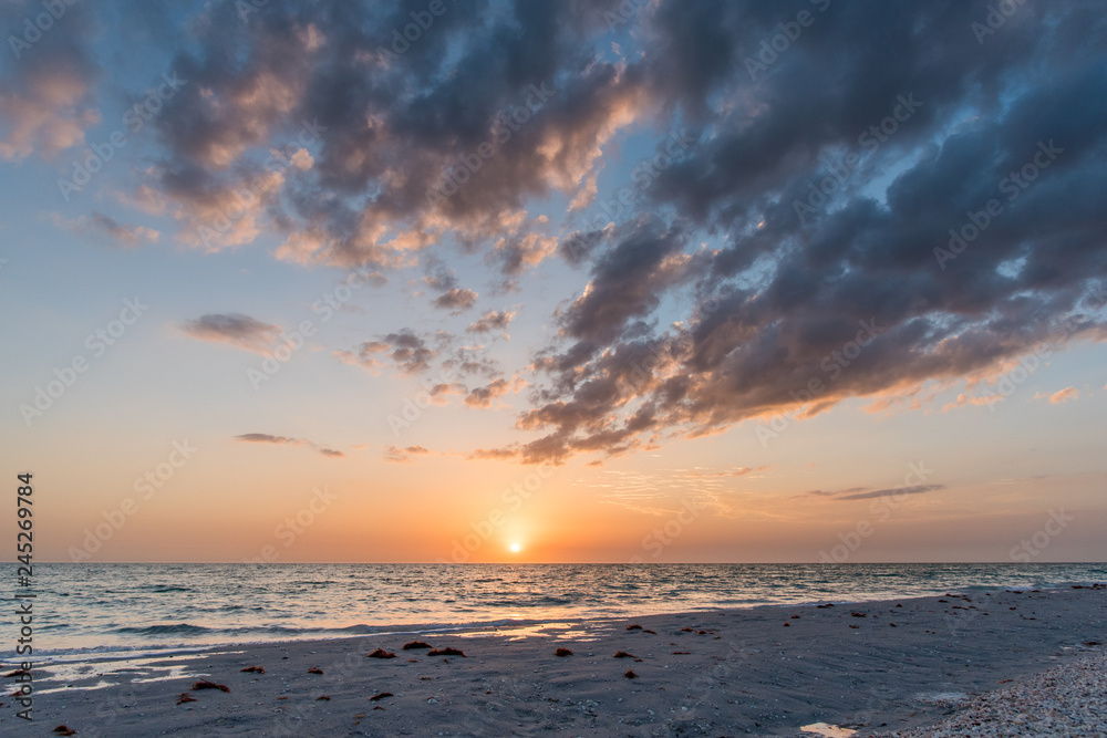 Sweeping Florida beach clouds over low tide with soft peach sunset 