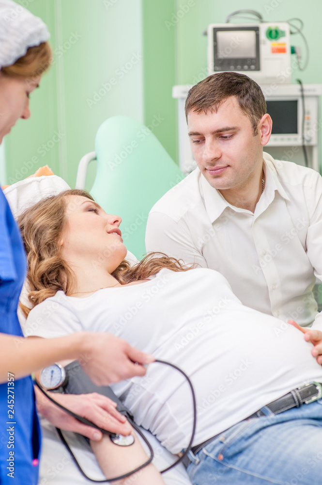 Obraz premium Nurse measuring pressure of pregnant woman. Husband supports pregnant wife for examination