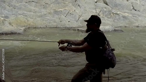 A fly fisherman is silhouetted against a roaring river while mending line in slow motion. photo