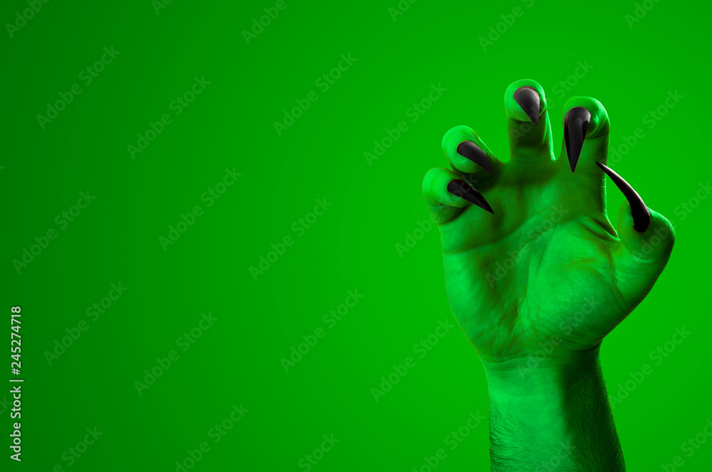 Halloween, nightmare creature and evil monster horror story concept with a scary zombie or demon hand with creepy long black nails isolated on green with a clip path cutout and copy space