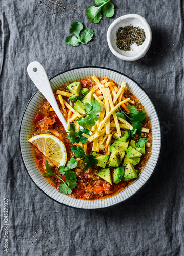 Crock pot vegetarian quinoa tomato soup with corn tortilla chips, avocado and cilantro on grey background, top view