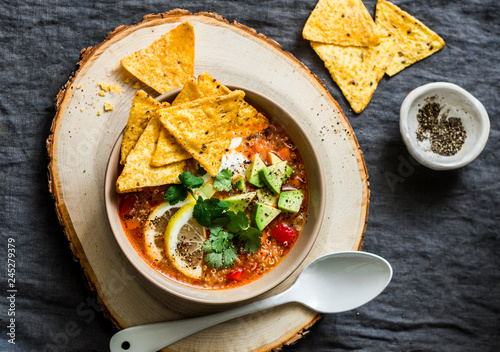 Vegetarian quinoa tomato soup with corn cheese chips, avocado and cilantro on grey background, top view photo
