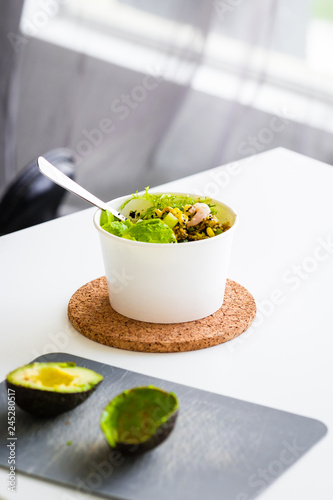 Take away salad in disposable white paper bowl on white table. Minimalism food photography concept. Mockup, copyspace, vertical