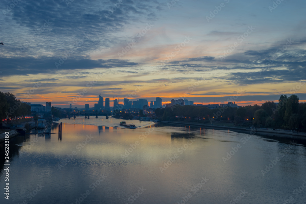 Paris, France - 11 04 2018: View of the towers of La Défense district from the Clichy bridge at sunset. A barge