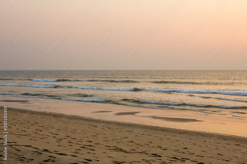 sandy beach with footprints on the background of the sea under a gray pink blue evening sunset sky