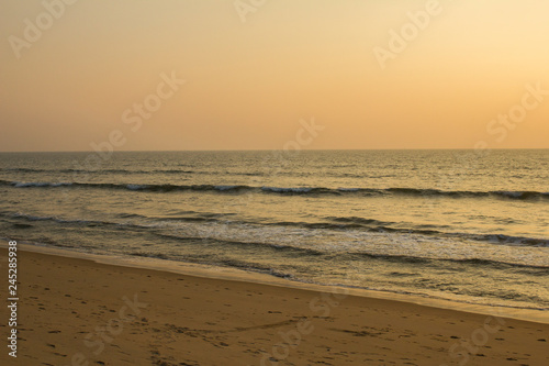 sandy beach with many footprints on the background of the waves of the ocean and the gray pink sky of sunset