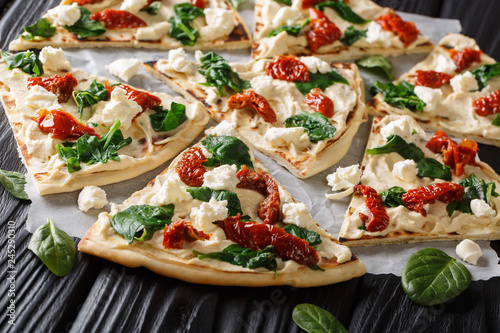 Delicious open sandwiches from flat bread with hummus, dried tomatoes, spinach and goat cheese close-up. horizontal photo