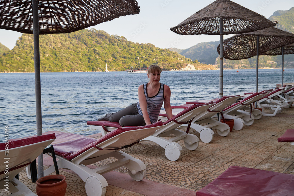 Middle-aged woman on a sunbed by the sea and mountains in the background