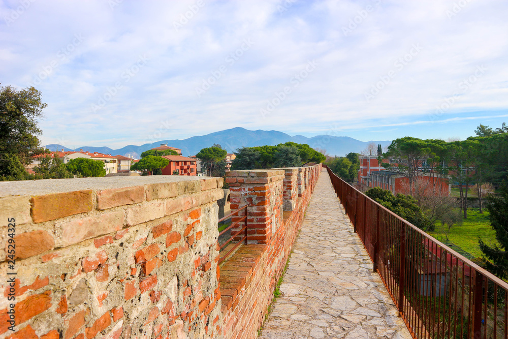 Red brick Pisa city wall walkway with Tuscany mountains and trees on the background, Italy