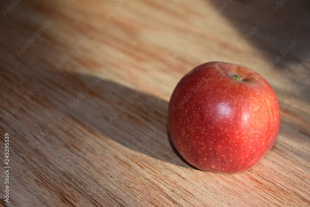Roter Apfel mit langen Schatten auf einem Holzbrett Roter Apfel mit langen Schatten auf einem Holzbrett
