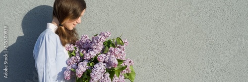 Young teen girl with bouquet of lilac near gray wall outdoor background, panoramic banner, girl in profile, copy space.