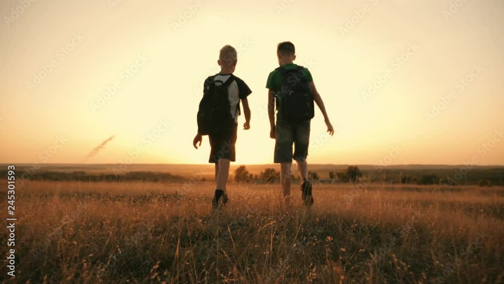 Two travelers boy. Two boys are walking along the field at sunset with rucksacks. The concept of family and travel Two travelers boy. Two boys are walking along the field at sunset with rucksacks. The concept of family and travel