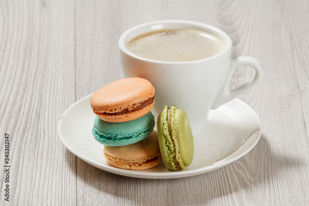 Cup of coffee and delicious macarons cakes of different color on white plate Cup of coffee and delicious macarons cakes of different color on white plate