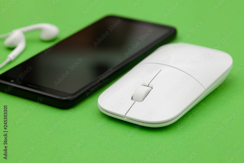 White wireless optical mouse with a wheel, black smartphone and headphones on a green background. Modern concept for the Internet web site. Free space for input text, image, and logo. Mockup White wireless optical mouse with a wheel, black smartphone and headphones on a green background. Modern concept for the Internet web site. Free space for input text, image, and logo. Mockup