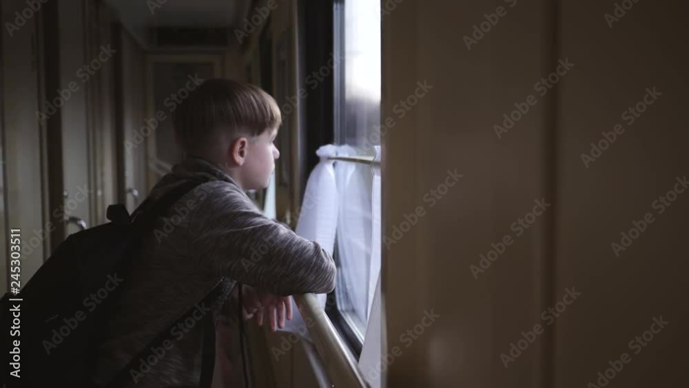 The boy stands at the train window and looks out the window at the running landscapes. Travel by train. Tourism on vacation, travel around the world. The boy stands at the train window and looks out the window at the running landscapes. Travel by train. Tourism on vacation, travel around the world.