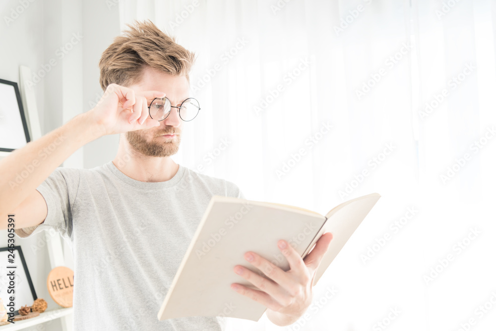 Handsome young caucasian Man reading a book in his living room ,feeling serious and surprised Handsome young caucasian Man reading a book in his living room ,feeling serious and surprised