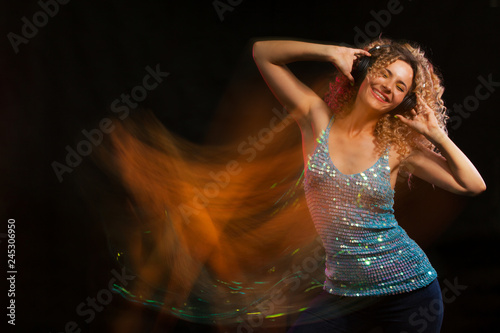 Attractive dancing woman with curly hair and red headphones in black background, neon light, motion effects. Copyspace, long exposure.