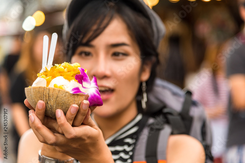 Closed up of cute girl teenage traveler eating enjoying coconut ice cream on the Thailand trip holiday in summer at local market street.