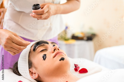 Close up of Healthy Young Woman getting mud Black facial mask cosmetic procedure in the beauty salon.Skin treatment in spa salon concept