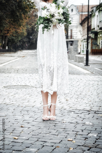 Bride in lace vintage dress and elegant high heels sandals holding bouquet with eucaliptus. Closeup, copy space