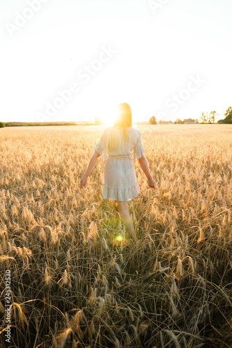 Romantic girl outdoors wandering through field feeling relaxed on a warm summer sunset