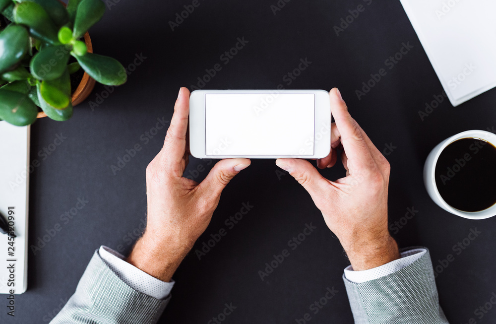 A midsection of businessman sitting at the table, using smartphone. A top view. Copy space. A midsection of businessman sitting at the table, using smartphone. A top view. Copy space.