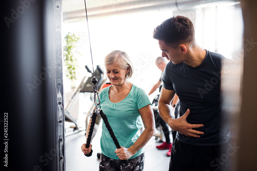 A female senior with a young trainer doing strength workout exercise in gym. photo