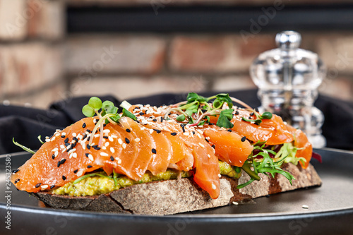 Close up view on sandwich with salmon, microgreen and avocado on a black plate. Healthy food for menu. Free copy space. Healthy diet background