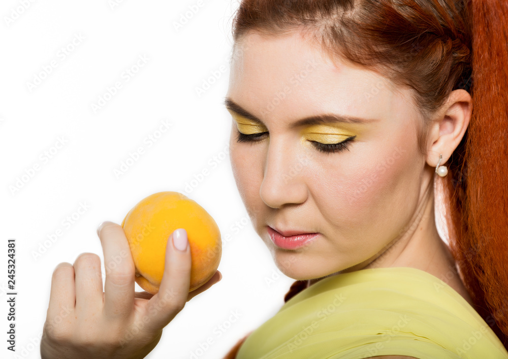Young redhead woman holding a peach near her face on a white background. Young redhead woman holding a peach near her face on a white background.