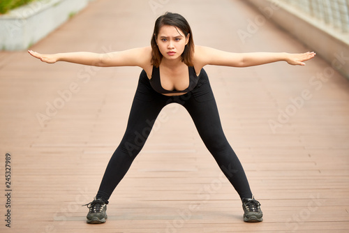 Focused Asian woman in sportswear doing yoga practice on paved wooden waterfront bending forward