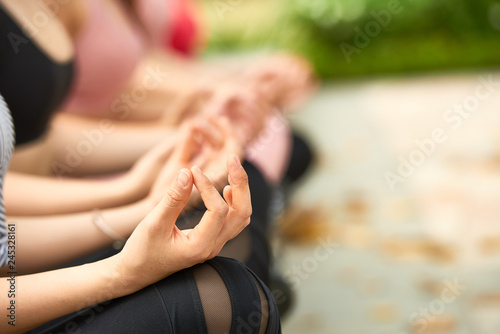 Crop side view of women sitting in row and meditating peacefully in city park