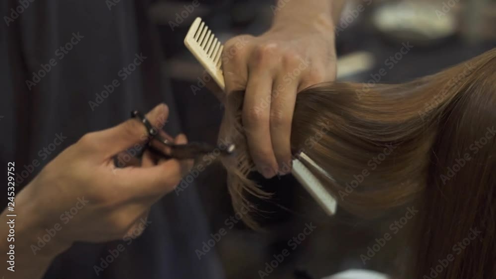Man hairstylist cutting hair with scissors in hairdressing studio. Female hairstyle in professional beauty salon. Hairdresser doing woman haircut in barbershop. Beauty and care.