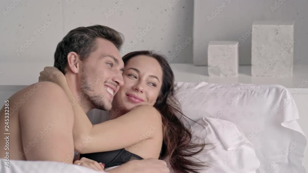 Happy loving couple embracing while lying together in bed at home Happy loving couple embracing while lying together in bed at home