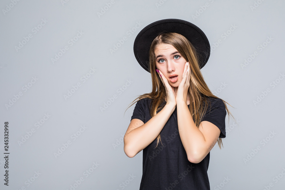 Close-up portrait of shocked attractive woman in black hat standing with opened palms, looking at camera, isolated on gray background