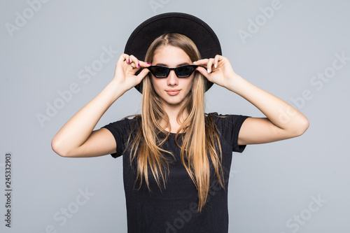 Fashion portrait pretty woman in black hat and sunglasses over grey background. Holiday concept