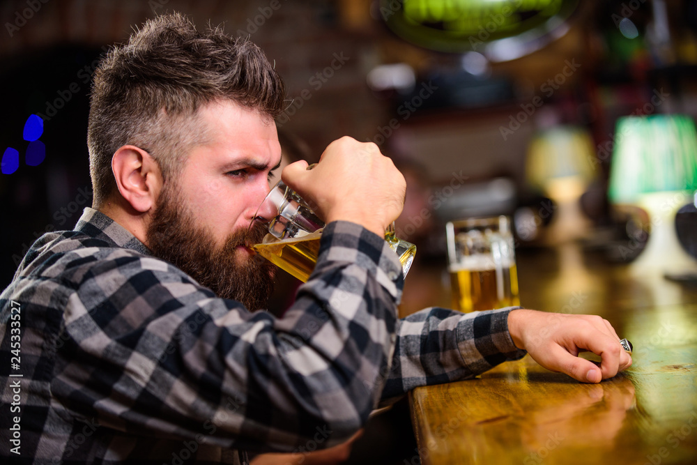 Order alcohol drink. Bar is relaxing place have drink and relax. Hipster relaxing at bar with beer. Man with beard spend leisure in dark bar. Brutal hipster bearded man sit at bar counter drink beer